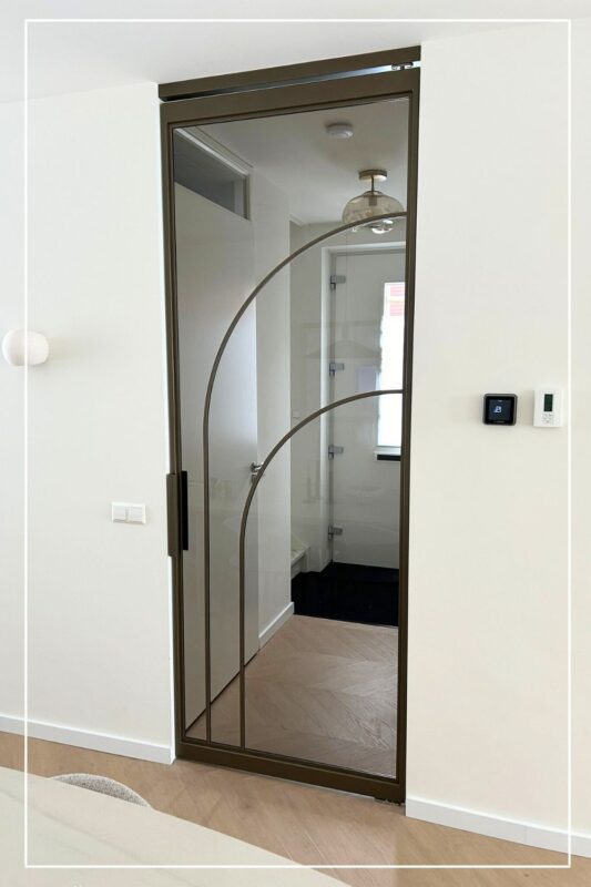 Skygate Flow enkele taatsdeur in bonded bronze afwerking, maatwerkdesign met organische profielen.