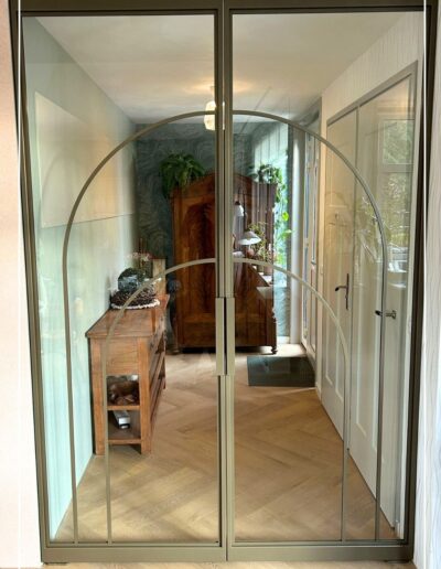 Skygate Flow symmetrische dubbele taatsdeuren met organische profielen en glas, geplaatst in een gang.