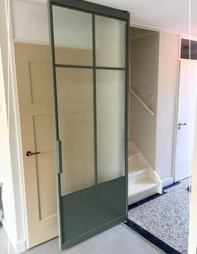 Groene stalen taatsdeur eigen design met ribbelglas van Skygate in een hal met trapopgang