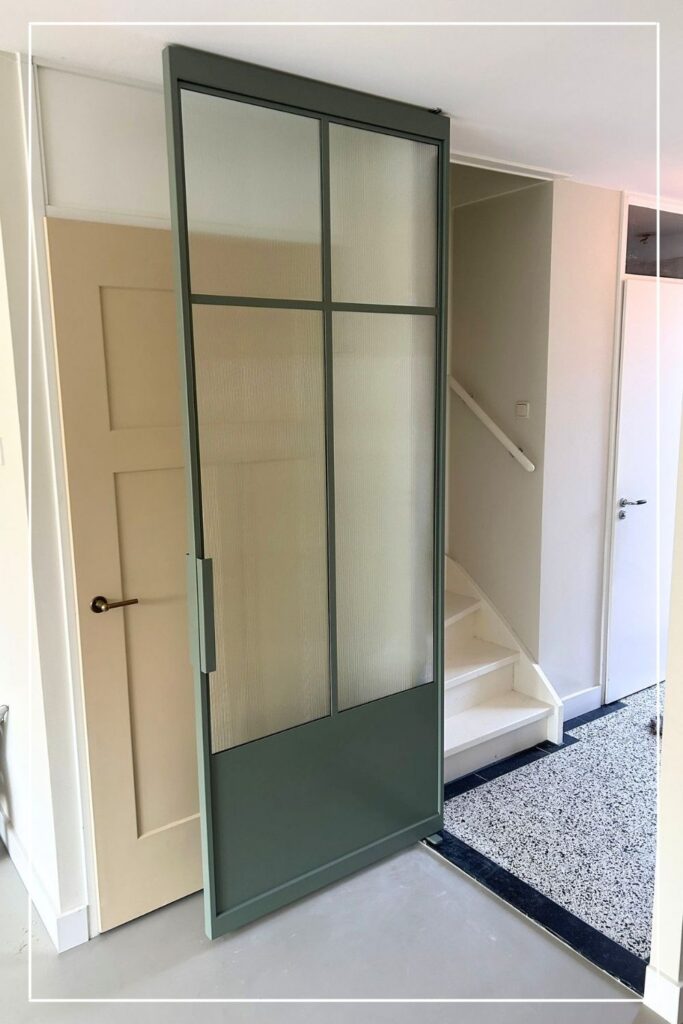 Groene stalen taatsdeur eigen design met ribbelglas van Skygate in een hal met trapopgang