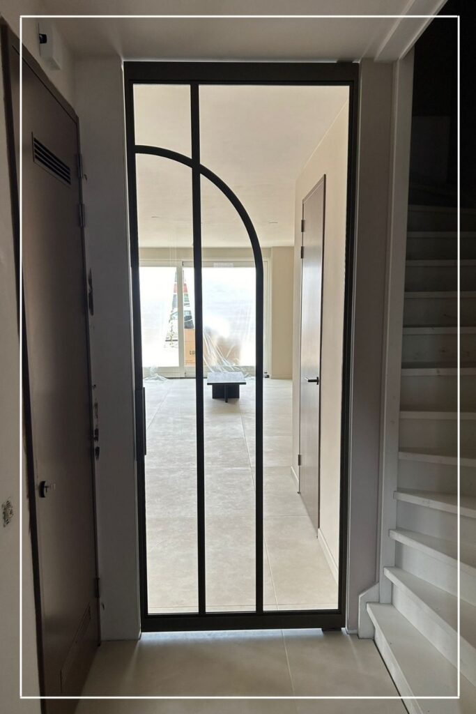 Hoge zwarte stalen taatsdeur met boogdesign en helder glas van Skygate in een hal